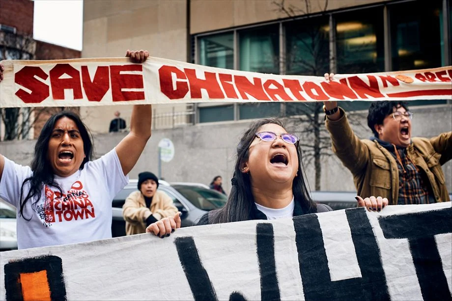 A group of people hold a banner that says "Save Chinatown" in red ink; the people are yelling as if in protest